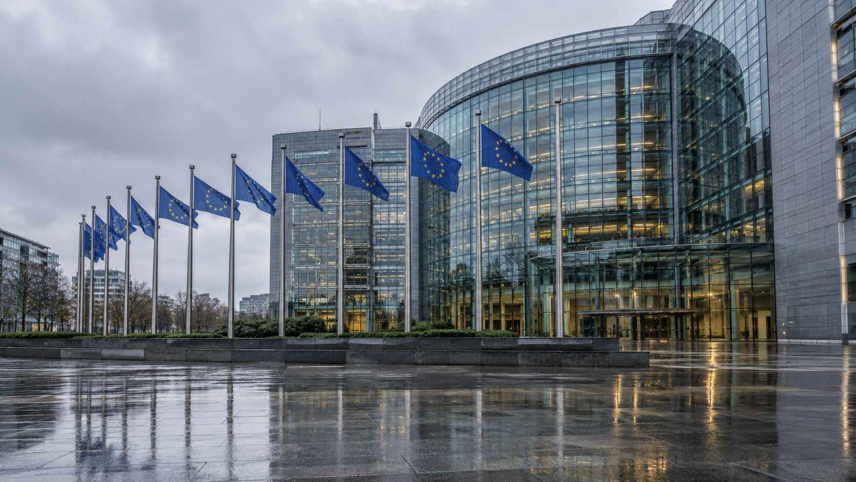 Façade vitrée d’un bâtiment institutionnel européen sous un ciel gris, rangée de drapeaux bleus et trottoir mouillé.
