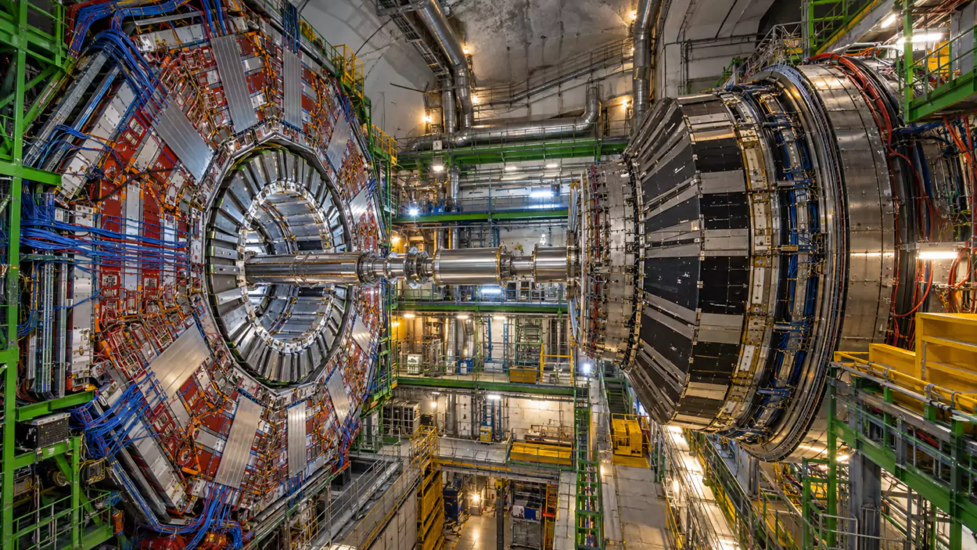 Vue large d’un détecteur de physique des particules dans sa caverne souterraine, cylindres d’acier et faisceaux de câbles.