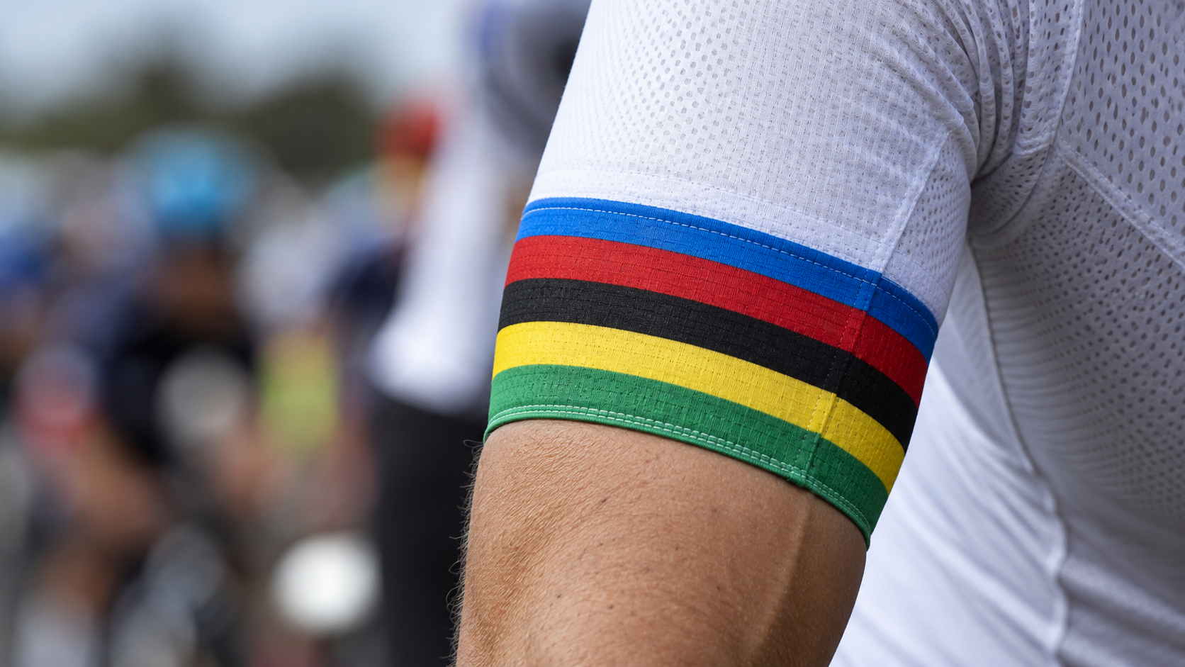 Gros plan sur cinq bandes bleue, rouge, noire, jaune et verte cousues sur la manche d'un maillot de cycliste.