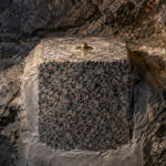 Bloc de granit poli scellé dans la roche d’une chambre souterraine, un petit rivet de bronze luisant à son sommet.