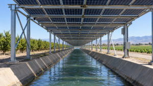Un canal d’irrigation rectiligne surmonté d’une charpente métallique couverte de panneaux solaires, au milieu de terres agricoles.