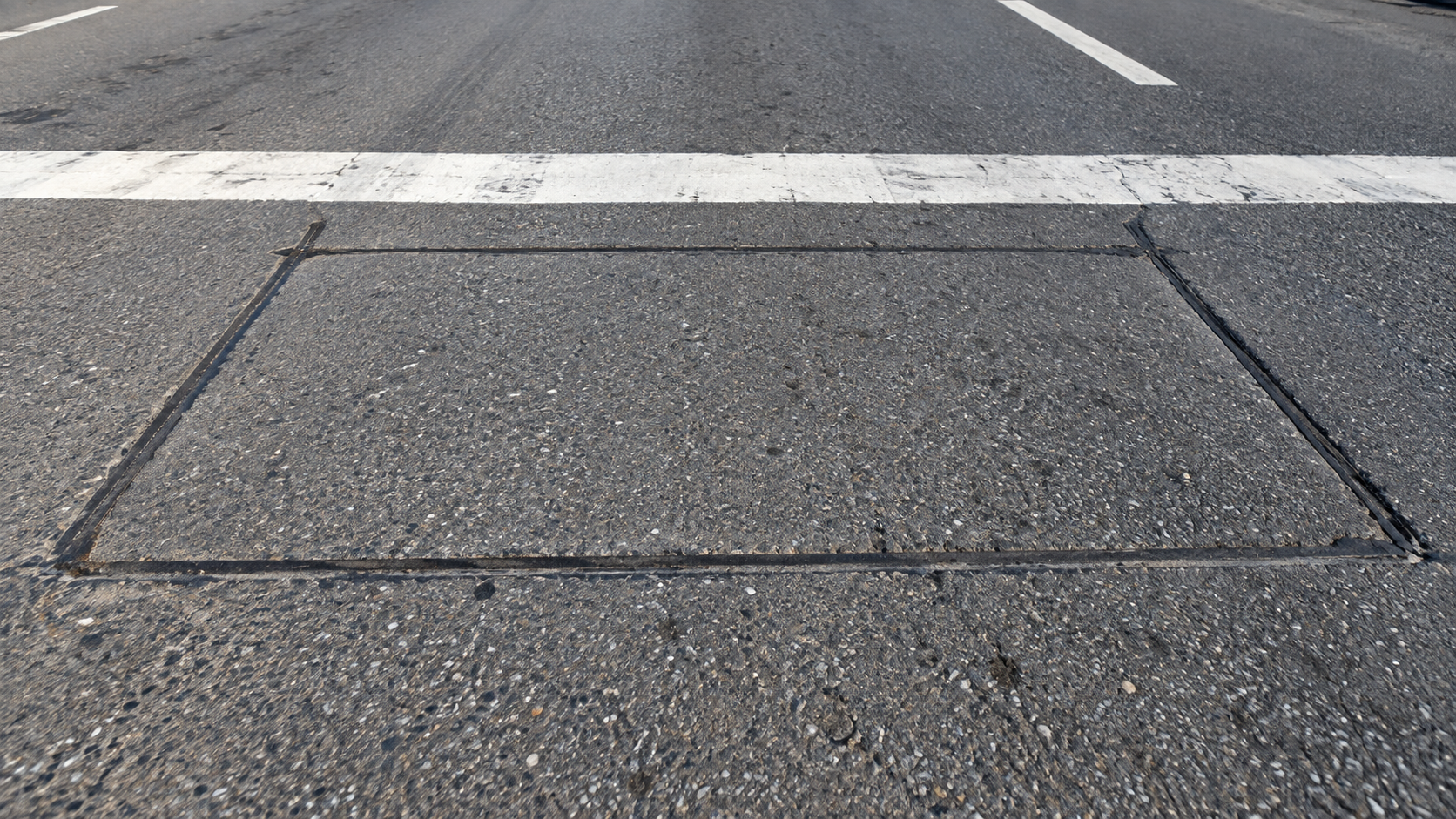 Les entailles rectangulaires d’une boucle de détection découpées dans l’asphalte, juste derrière une ligne d’arrêt blanche.
