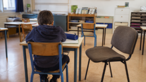 Salle de classe vide d’une école primaire française, une chaise d’adulte inoccupée placée contre un pupitre d’élève.