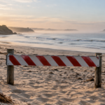 Plage australienne déserte au matin, barrière de fermeture plantée dans le sable devant une mer calme.
