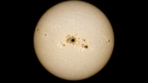 Gros plan du disque solaire en lumière blanche, vaste groupe de taches sombres près de l’équateur sur une photosphère granuleuse.