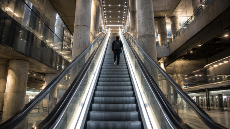 Un voyageur de dos monte un long escalator éclairé dans une station de RER aux piliers de béton.