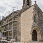 Chapelle de village sous échafaudage, une partie de la pierre nettoyée, l’autre encore grise.