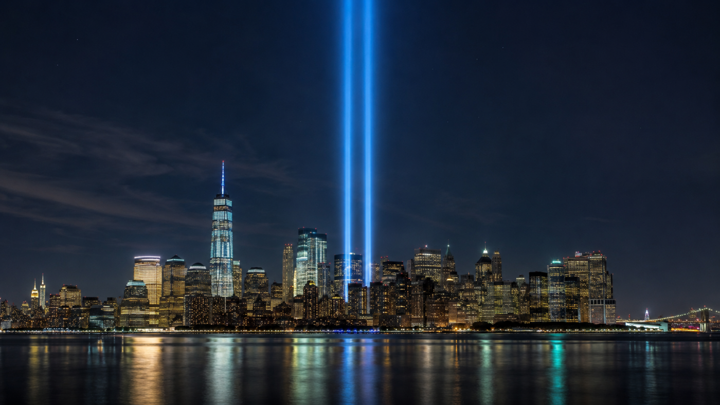 Deux colonnes verticales de lumière bleue s’élevant au-dessus d’une skyline américaine dense, vues de nuit depuis l’autre rive d’un fleuve calme.