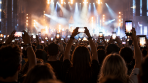 Une foule de concert vue de dos, smartphones levés vers une scène éclairée