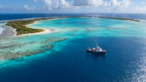 Lagon turquoise d’un atoll désert du Pacifique vu du ciel, un petit navire de recherche à l’ancre au large