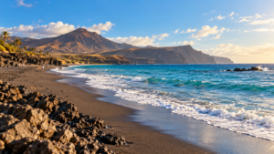 Plage de sable volcanique aux Canaries sous un soleil d’après-midi, quelques promeneurs au loin sur le rivage