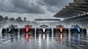 Cinq monoplaces de Formule 1 sans marque côte à côte, quasiment à l'arrêt sur une ligne droite détrempée sous un ciel gris